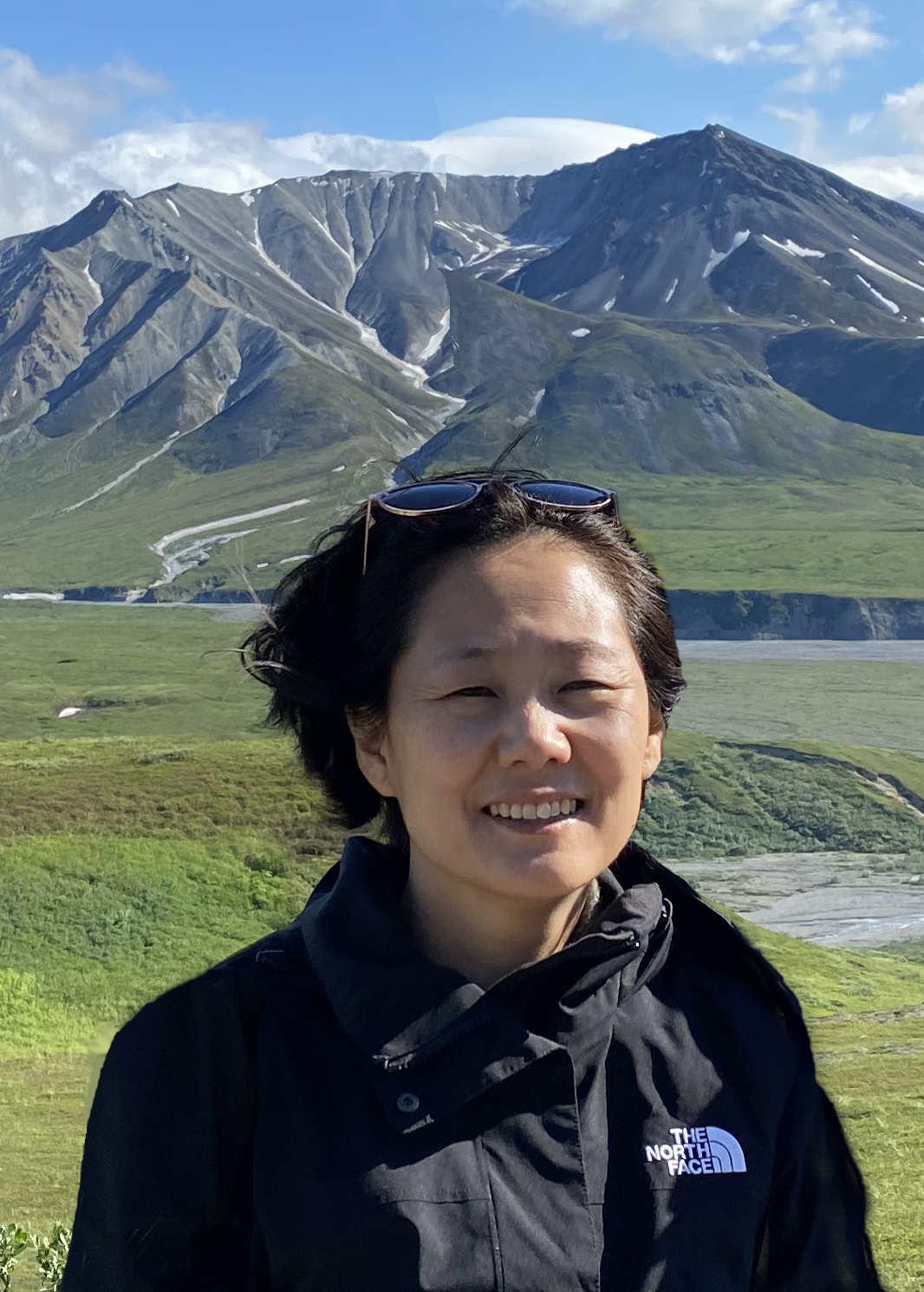 Illustrator YoungJu Kim in front of mountains wearing black windbreaker.